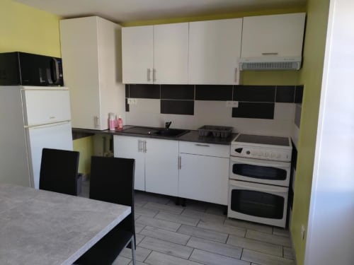 Kitchenette moderne à l'Appart'Hôtel Cholet avec placards blancs, crédence noire, double four et table à manger
