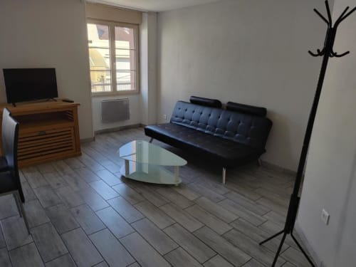 Salon de studio à l'hôtel Cholet avec canapé noir, table en verre, meuble TV en bois et accès au balcon