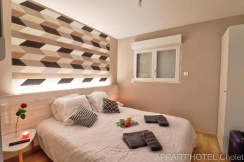 Chambre moderne à l'Appart'Hôtel Cholet avec tête de lit géométrique, literie blanche et décoration contemporaine