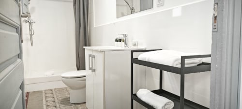 Baño moderno en apartamento del Eixample de Barcelona con inodoro, lavabo y estantería negra con toallas enrolladas