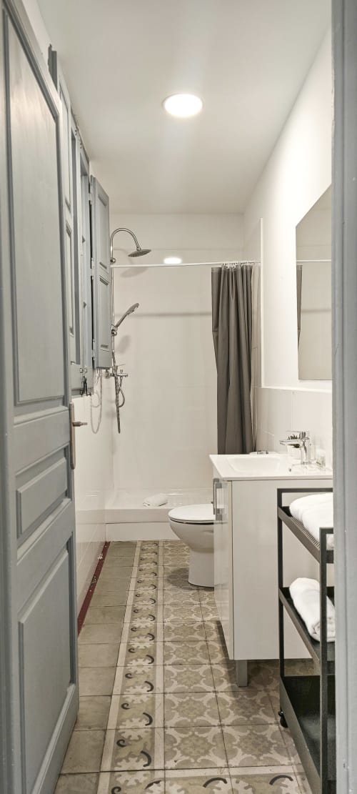 Baño moderno en apartamento BCNMADflats Barcelona con ducha tipo lluvia, lavabo blanco, inodoro y suelo con patrón