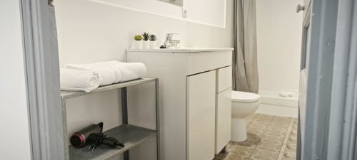 Baño moderno en apartamento del Eixample barcelonés con vanidad blanca, inodoro, toallas enrolladas y decoración minimalista