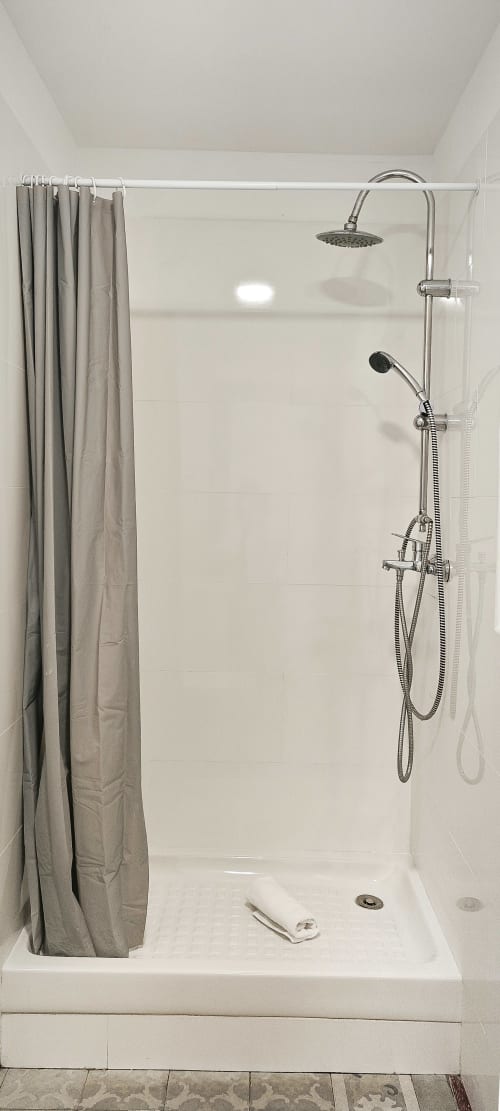 Moderna cabina de ducha con alcachofa de lluvia, rociador manual, azulejos blancos y cortina gris en apartamento de Barcelona