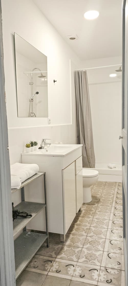 Baño moderno en apartamento del Eixample barcelonés con lavabo blanco, espejo, ducha, inodoro y baldosas decorativas