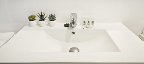 Moderno lavabo con encimera blanca, grifo, suculentas y artículos de tocador en apartamento de Barcelona