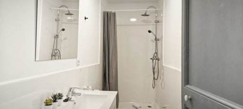 Baño moderno en apartamento del Eixample de Barcelona con doble lavamanos, espejos amplios y ducha contemporánea