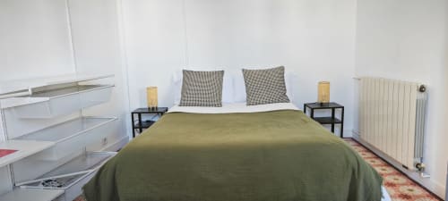 Dormitorio moderno en apartamento de Barcelona Eixample con colcha verde oliva, almohadas estampadas, mesillas negras y paredes blancas