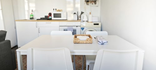 Zona de cocina-comedor moderna en apartamento de Barcelona Eixample con mesa blanca, sillas y electrodomésticos