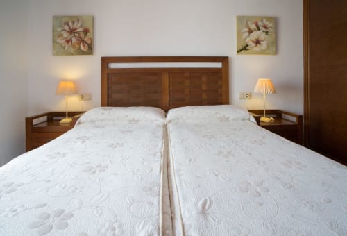 Spacious double bedroom at Alojamientos Carolina y Vanesa with two white quilted beds, wooden headboard, bedside lamps, and