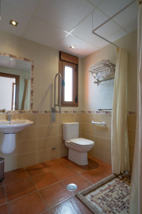 Modern bathroom with terracotta tiles, beige wall tiles, pedestal sink, toilet, shower with curtain, and mirror at