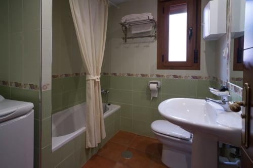 Green-tiled bathroom with white sink, toilet, bathtub with shower curtain at Alojamientos Carolina y Vanesa, San José