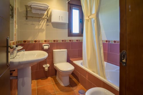 Bathroom at Alojamientos Carolina y Vanesa with terracotta tiles, white sink, toilet, bathtub with shower curtain, and