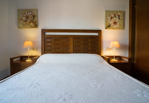 Double bedroom with white quilted bed, wooden headboard, bedside lamps, and floral wall art at Alojamientos Carolina y