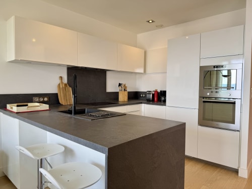Cuisine blanche moderne avec îlot aux comptoirs sombres, appareils inox et bar, appartement SoleMare Alata
