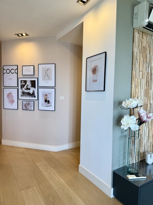 Couloir moderne de l'appartement SoleMare avec galerie murale encadrée, murs blancs, parquets et fleurs fraîches sur table de présentation