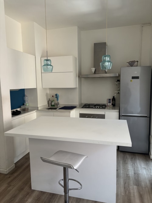 Modern white kitchen with island, stainless steel appliances, pendant lights, and bar seating at Milano Underground apartment