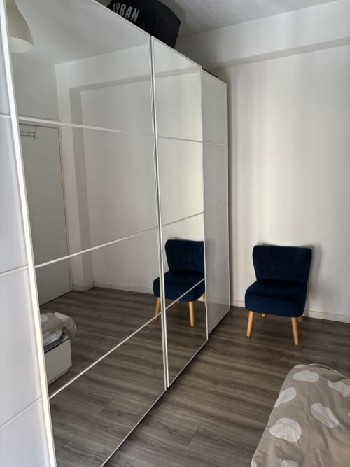 Modern bedroom in Milano Underground apartment with mirrored wardrobe, dark blue chair, and wooden flooring