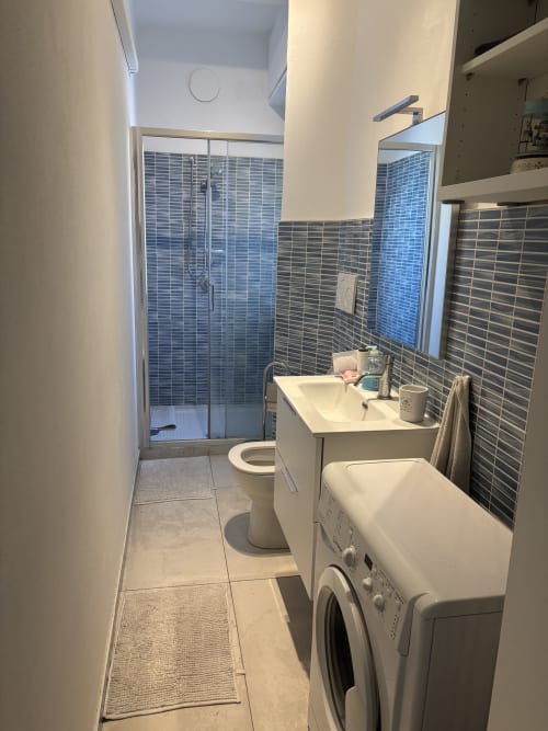 Modern bathroom with shower, sink, toilet, and washing machine in Milano Underground apartment