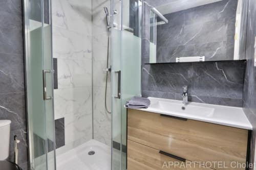 Salle de bain moderne du studio Appart'Hôtel Cholet avec carrelage marbre, douche vitrée, meuble vasque bois et lavabo blanc