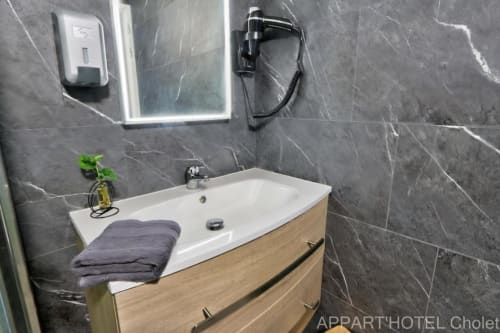 Salle de bain moderne de l'Appart'Hôtel Cholet avec murs en marbre gris, lavabo blanc, meuble de rangement en bois et équipements hôteliers