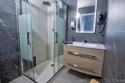 Salle de bain moderne à l'Appart'Hôtel Cholet avec murs en marbre gris, douche vitrée et vasque en bois