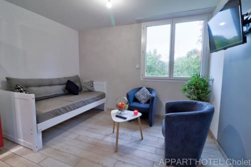 Espace lounge moderne à l'Appart'Hôtel Cholet avec canapé-lit, fauteuils, TV et vue sur le jardin