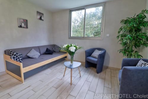 Salon moderne de l'Appart'Hôtel Cholet avec canapé, fauteuils, table basse blanche et vue sur le jardin