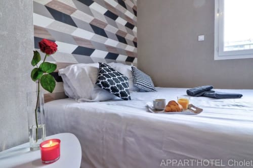 Chambre moderne à l'Appart'Hôtel Cholet avec tête de lit géométrique, rose rouge, plateau petit-déjeuner et coussins à motifs