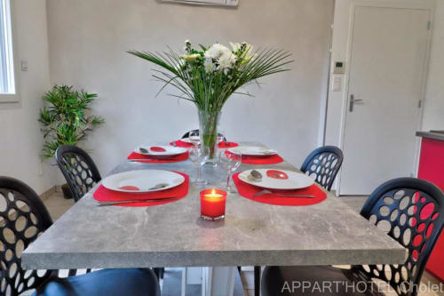 Table de salle à manger élégamment dressée à l'Appart'Hôtel Cholet avec fleurs blanches, set de table rouge et chaises noires modernes.