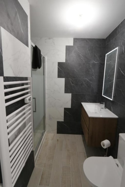 Salle de bain moderne de l'Appart'Hôtel Cholet avec carrelage marbre noir et blanc, sèche-serviettes chauffant, miroir lumineux