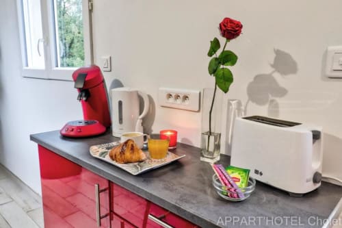 Kitchenette moderne à l'Appart'Hôtel Cholet avec cafetière rouge, grille-pain, croissant frais et rose rouge sur le comptoir