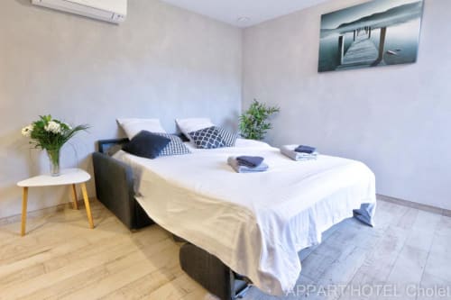 Chambre moderne à l'Appart'Hôtel Cholet avec lit queen-size, literie blanche, coussins décor et plantes, décoration style lac