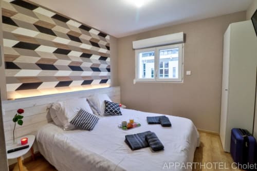 Chambre moderne de l'Appart'Hôtel Cholet avec tête de lit géométrique, literie blanche et vue sur fenêtre