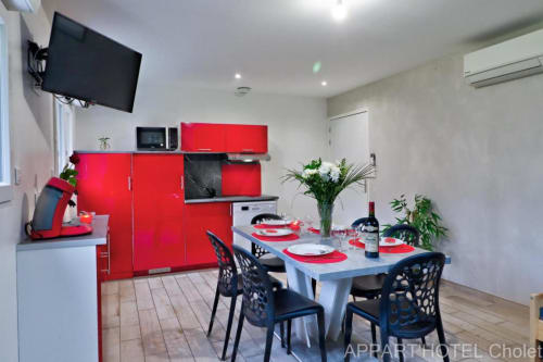 Cuisine et coin repas modernes de l'Appart'Hôtel Cholet avec meubles rouges, table à manger et télévision