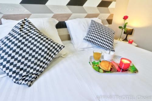 Chambre d'Appart'Hôtel Cholet avec plateau-petit-déjeuner, oreillers noir et blanc, rose et bougie de nuit