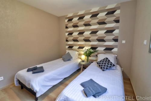 Deux lits jumeaux dans la chambre moderne de l'Appart'Hôtel Cholet avec mur d'accent géométrique