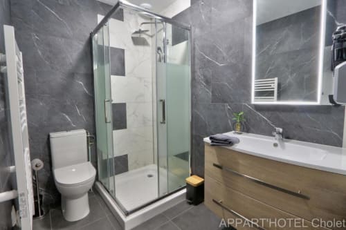 Salle de bain moderne de studio Appart'Hôtel Cholet avec carrelage marbre gris, douche vitrée, meuble vasque bois, toilettes