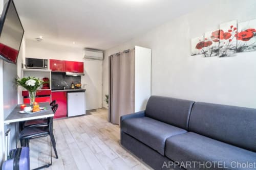 Studio de l'Appart'Hôtel Cholet avec kitchenette rouge, table à manger, canapé-lit gris et vue jardin