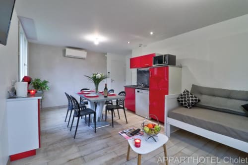 Appartement 3 chambres moderne à l'Appart'Hôtel Cholet avec cuisine rouge, salle à manger et canapé gris dans un espace ouvert