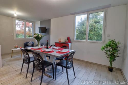 Coin salle à manger du studio 2 chambres avec vue sur jardin à l'Appart'Hôtel Cholet, table rouge design contemporain