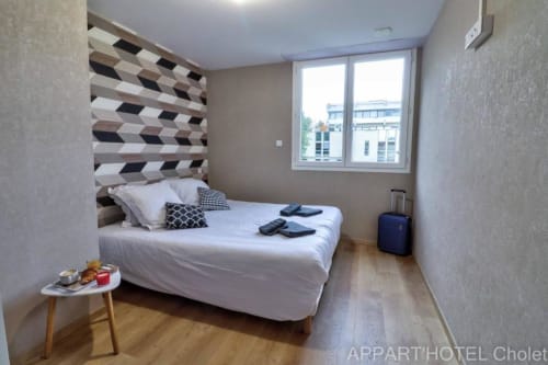 Chambre moderne de l'Appart'Hôtel Cholet avec lit queen-size, tête de lit géométrique et vue sur le jardin
