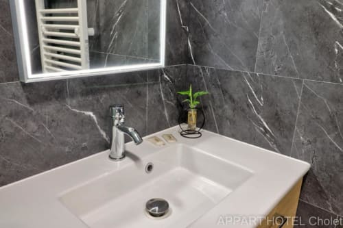 Lavabo moderne avec robinetterie chromée, vasque blanche et carrelage en marbre foncé à l'Appart'Hôtel Cholet, avec éclairage LED