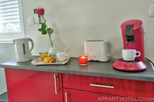 Coin cuisine de l'Appart'Hôtel Cholet avec cafetière rouge, bouilloire blanche et rose rouge fraîche en vase
