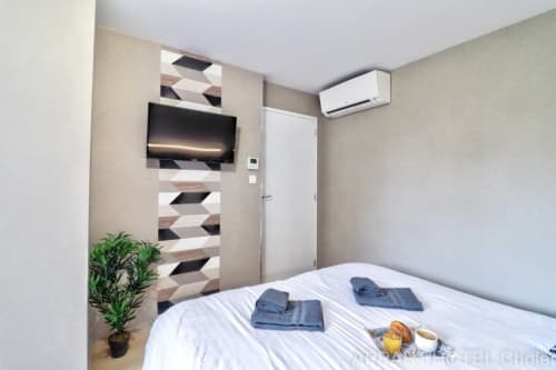 Chambre moderne à l'Appart'Hôtel Cholet avec télévision écran plat, climatisation, lit blanc, décoration murale géométrique et plante verte