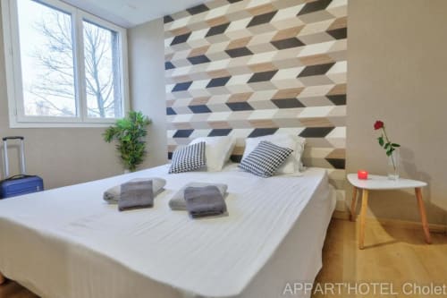 Chambre moderne à l'Appart'Hôtel Cholet avec tête de lit géométrique, lit blanc, oreillers à carreaux et vue sur jardin