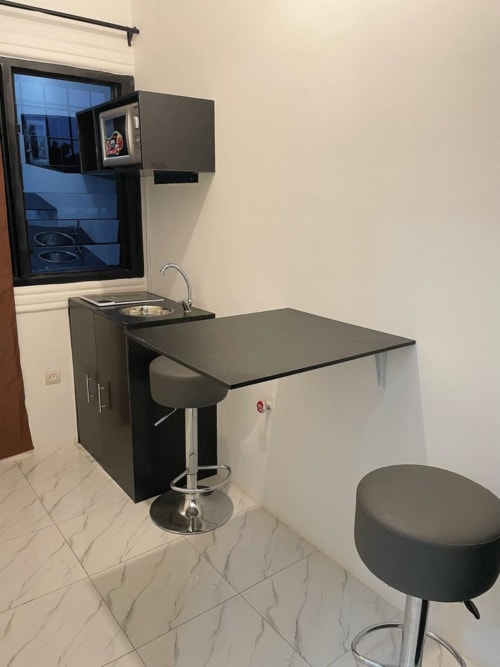 Mini-suite kitchenette moderne avec comptoir noir, évier, bar et tabouret à la Résidence hôtelière Ôkèrè Ôburu à Lomé