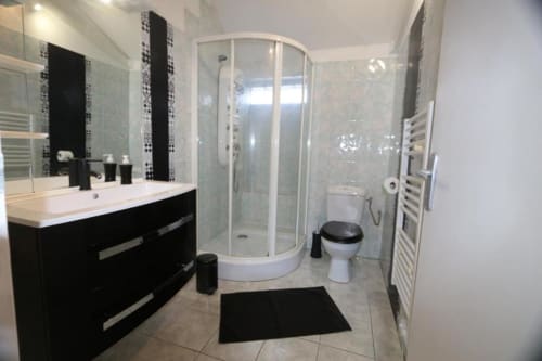 Salle de bain moderne à l'Appart'Hôtel Cholet avec meuble vasque noir, cabine de douche incurvée, toilettes et sèche-serviettes électrique
