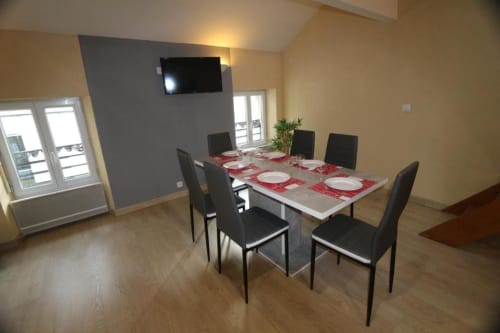 Salle à manger moderne dans l'appartement de l'Appart'Hôtel Cholet avec table, chaises noires, TV et fenêtres