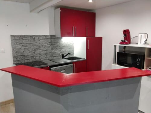 Cuisine moderne rouge et grise dans l'appartement 2 chambres d'Appart'Hôtel Cholet avec cuisinière, micro-ondes et comptoir repas