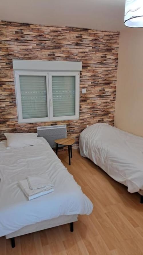 Twin bedroom in Appart'Hôtel villa, Cholet. Two single beds with white linens, wooden flooring, brick feature wall, and large